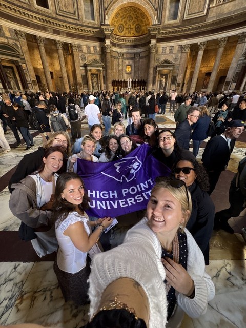 HPU students holding a High Point University flag inside the Pantheon in Rome