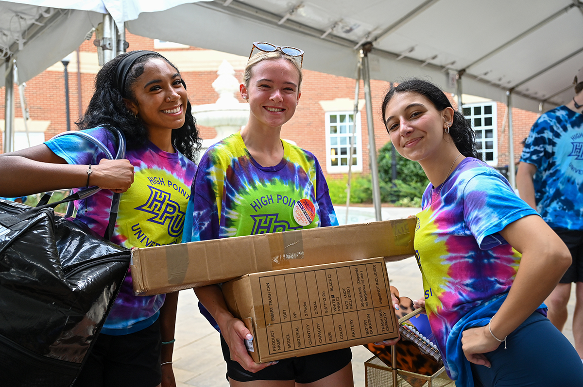 As is tradition, student volunteers dressed in tie-dyed T-shirts swiftly unloaded vehicles and helped move new students into their residence halls. Three student volunteers smiled while unloading a car.