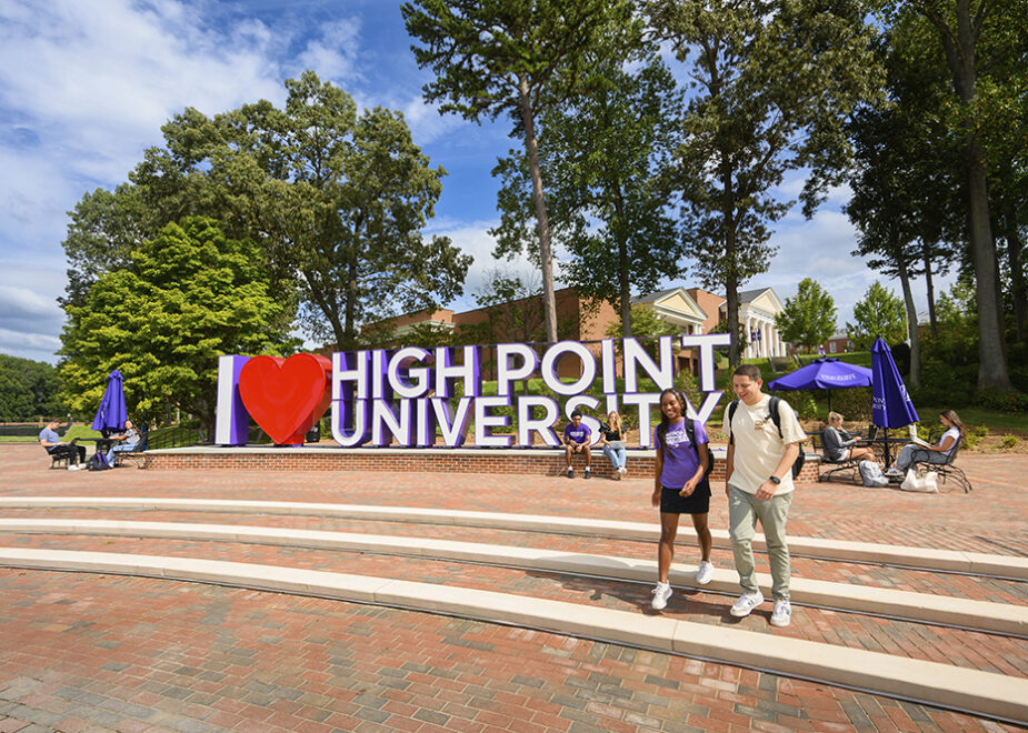 Two High Point University students walk past a large sign that reads, 