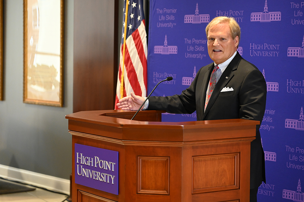 High Point University alumna Doug Witcher standing at a podium during the naming ceremony for the Douglas S. Witcher School of Humanities and Behavioral Sciences.
