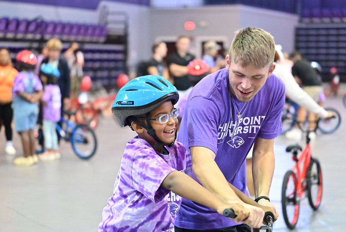 A child smiles as an HPU freshman helps him ride a new bike. 