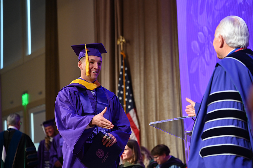 A graduate extended his hand to give Dr. Qubein a handshake after receiving his degree on stage.