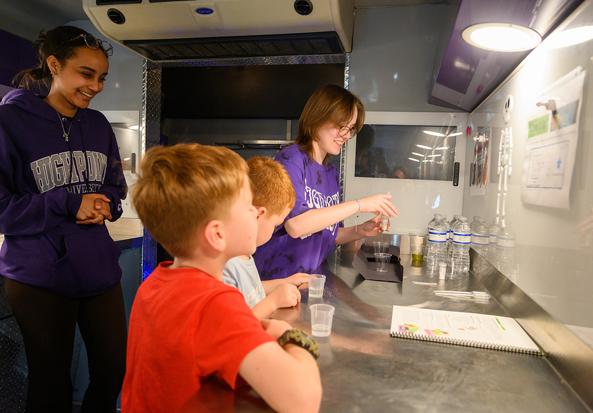 HPU students, Youliana Hadgu, left, and Julia Crenshaw, right, led bioluminescence activities for two boys inside the HPU Mobile Community Lab.