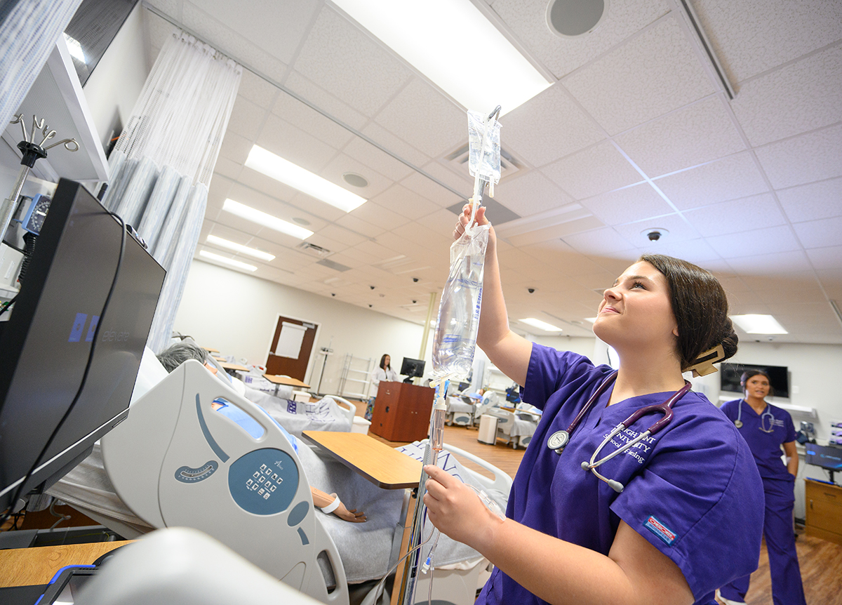 Katie Gaines smiles as she starts an IV drip in an HPU nursing simulation lab.