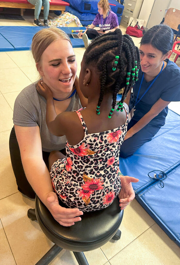 Pictured from left are Gabrielle Axson, a student physical therapist, working with a child in Belize. HPU PT student Angie Macchio is pictured next to them with Lila Campbell in the background.