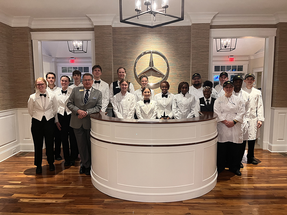 HPU students Dru Daniels, far left, Evan Petrocelli, third from the left in the back row, and Kailey Wrege, fifth from the left in the back row in front of the Mercedes symbol, served in a hospitality role at The Masters in 2024.
