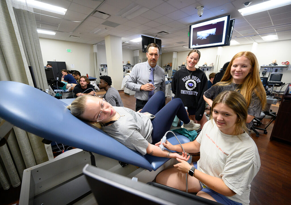 DPT student Michaela Morgan, on the table, had her wrist scanned by Elizabeth Underwood during a training session. Pictured standing behind them were Savage, with DPT students Sara Bittence and Riley Walsh.