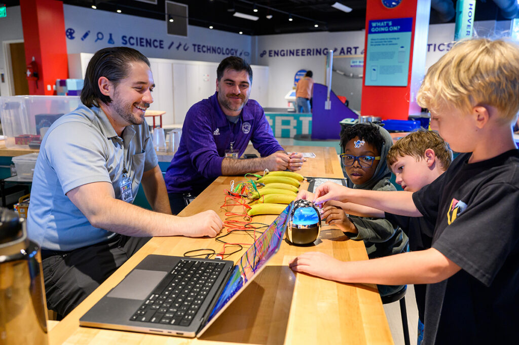 Dr. Jacob Brooks, interim chair and assistant professor of physics, and Dr. Eric Rokni, assistant professor of physics, smiled as they watched children react to banana piano acoustics.