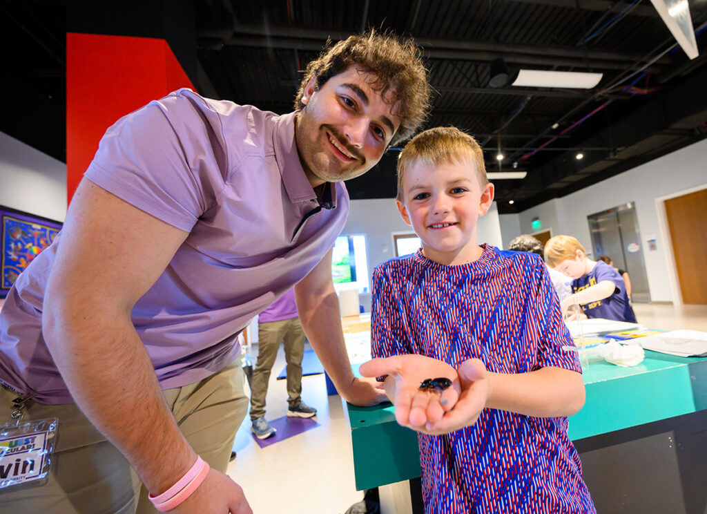 Gavin Agahigian, a junior biology major, smiled along with a boy who held a bug in the insect petting zoo.