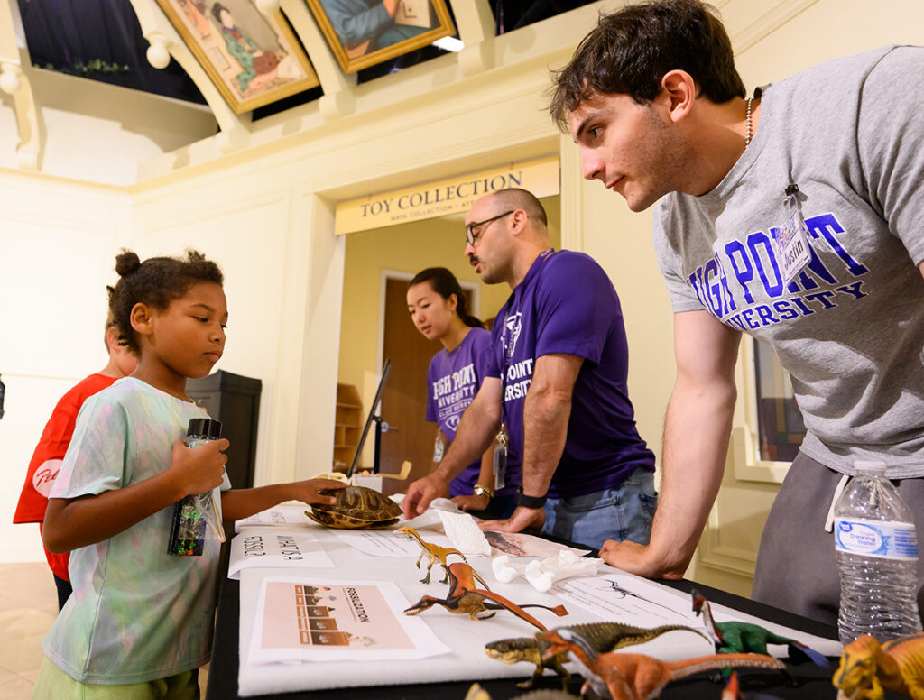 ) A child touched a turtle shell and considered dinosaur fossils as he talked with Justin Allan, a junior biology major. Behind him were Eleanor Lee, a sophomore biology major, and Dr. Josef Stiegler, assistant professor of biology.