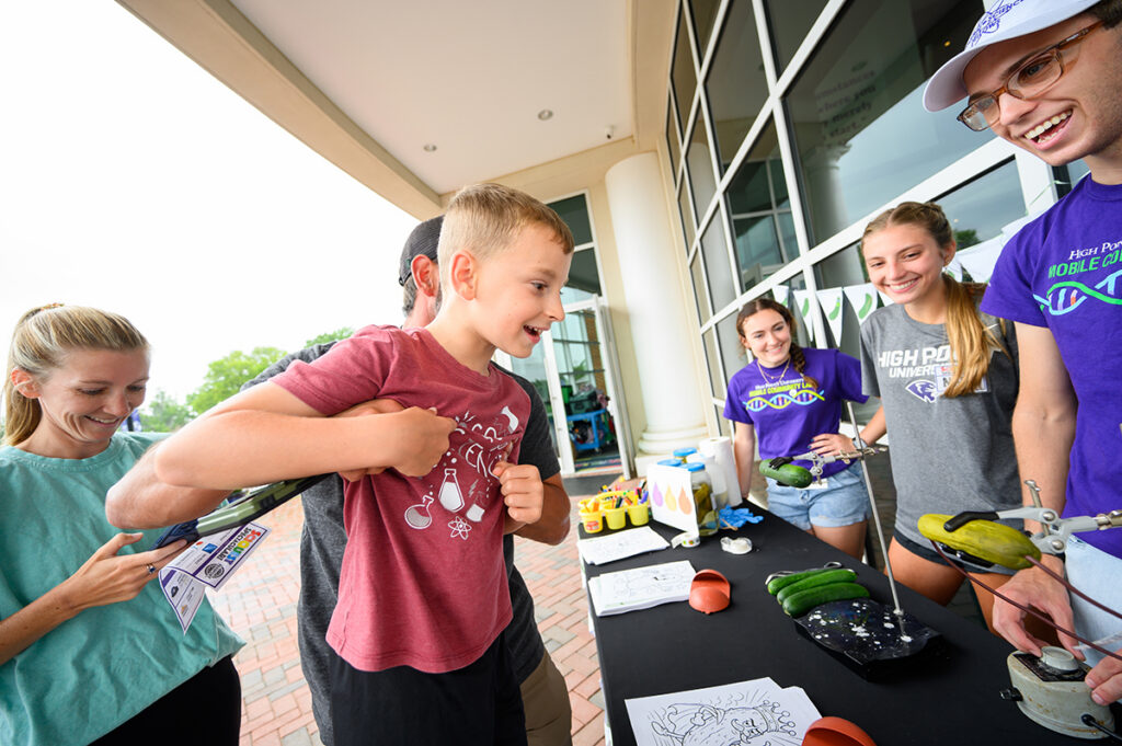 A father lifted his 7-year-old son for a clearer view of the electric pickles experiment on the museum’s front patio staffed by HPU students Sophia Messerly, a sophomore biochemistry major; Nelia Kelleher, a sophomore biology major, and Trip Donaldson, a sophomore chemistry major.