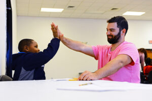 Beta Theta Pi member Sammy Bozza shares a high five with a student at Macedonia for completing a vocabulary activity.