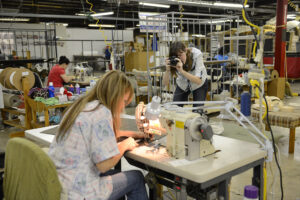 The photo features HPU student Stephanie Sapp photographing Braxton Culler employee Theresa Ernhart as she is sewing
