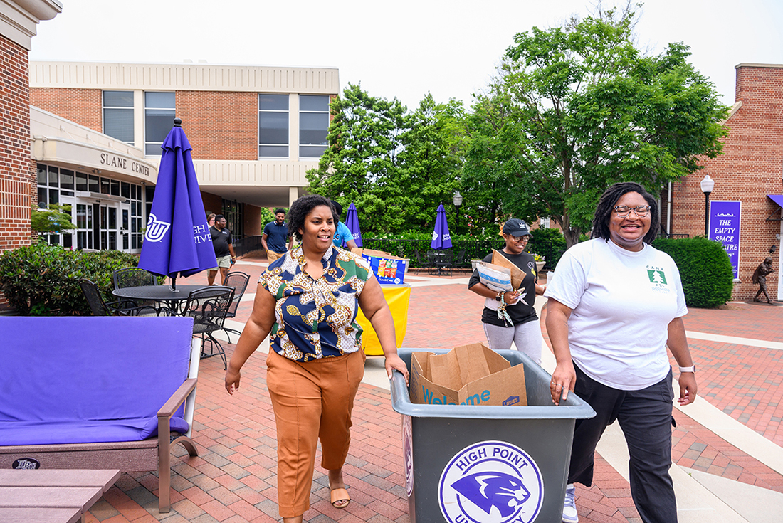 Crystal Harvey, HPU’s director of Residence Life, and Alyvia Williams, HPU assistant director of Residence Life, smile as they wheel a bin filled with nonperishable food toward the postal truck.
