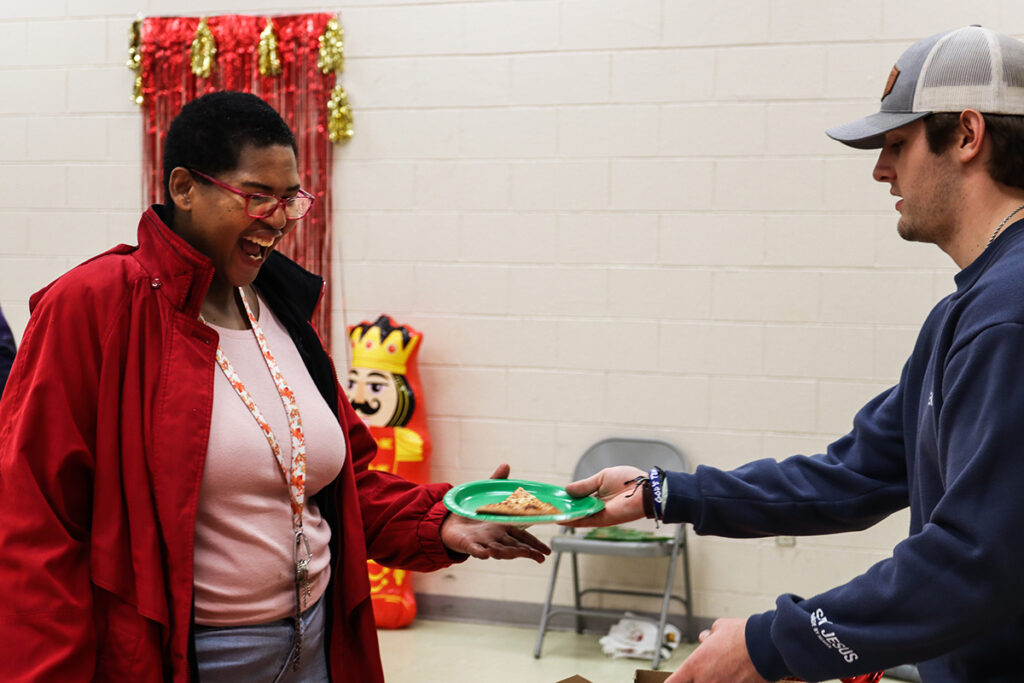 At right, Walker Ripley, a secondary education and history major from Steamboat Springs, Colorado, delights a community member by sharing a slice of pizza.