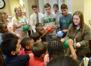 HPU student Olivia Scarborough, far right, conducts an experiment about polymers by inserting a skewer through a balloon without popping it.