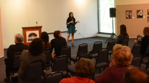 The photo features HPU student Cristy Hernandez discussing her experiences with the service learning class, “Documenting the Community through Photography.”