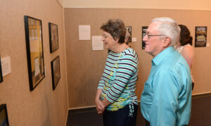 The photo features community members Neil and Jill Sheppard viewing the photographs at the exhibit.