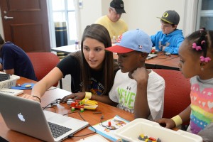 The photo features HPU student Amy Jamil helping participants of the Lego Day build with Legos.