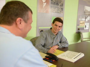 The photo features David Holmes helping a community member through the tax filing process. 