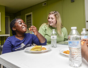 Kirkman Park Elementary School student Serenitee Broughton (left) enjoys a snack donated by Walmart with HPU student Katie O’Sullivan (right). 
