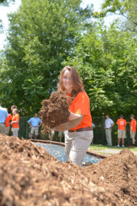 The photo features Youth Leadership Academy student Marissa Salvaterra spreading mulch on the playground at West End Ministries.